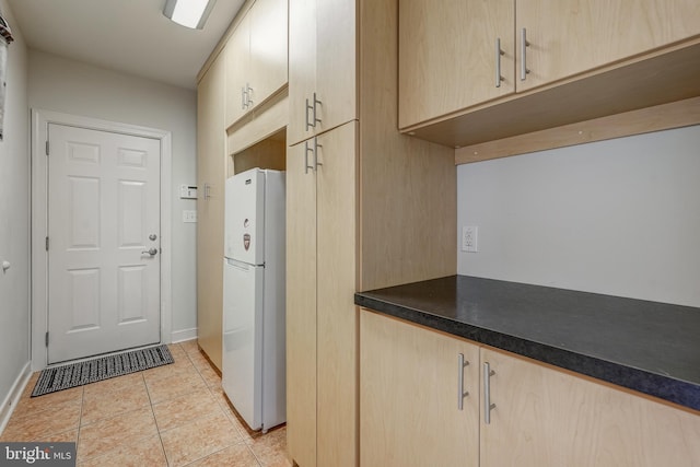 kitchen featuring dark countertops, light tile patterned floors, light brown cabinetry, and freestanding refrigerator