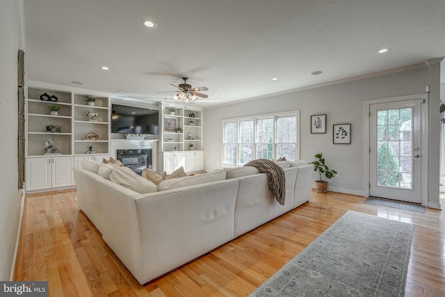 living area featuring a wealth of natural light, a glass covered fireplace, crown molding, and light wood finished floors