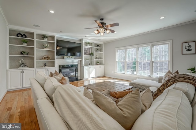 living area with recessed lighting, a fireplace, crown molding, and light wood finished floors