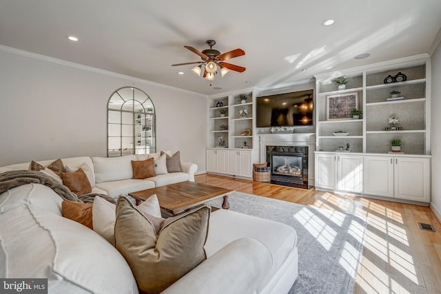 living room featuring light wood finished floors, a glass covered fireplace, visible vents, and crown molding