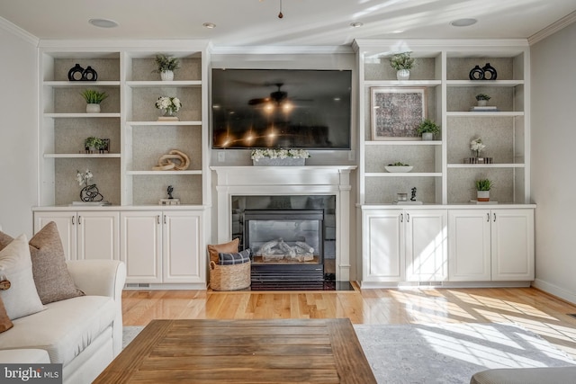 living room with a fireplace with flush hearth, built in shelves, ornamental molding, and light wood finished floors