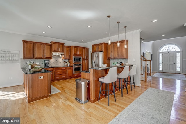 kitchen featuring a peninsula, under cabinet range hood, appliances with stainless steel finishes, and brown cabinetry