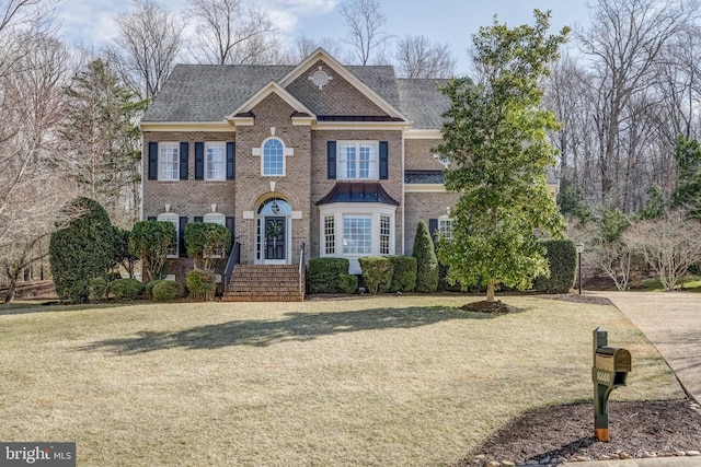 colonial inspired home featuring a front yard, brick siding, and roof with shingles