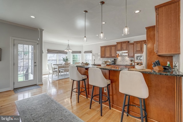 kitchen with stainless steel microwave, tasteful backsplash, brown cabinetry, and light wood finished floors