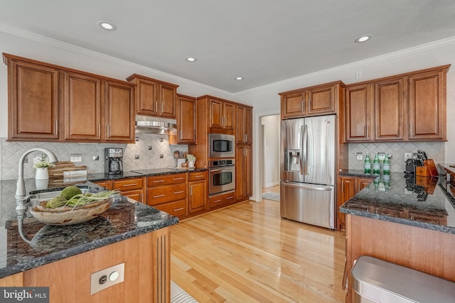 kitchen with stainless steel appliances, dark stone counters, brown cabinets, and light wood finished floors