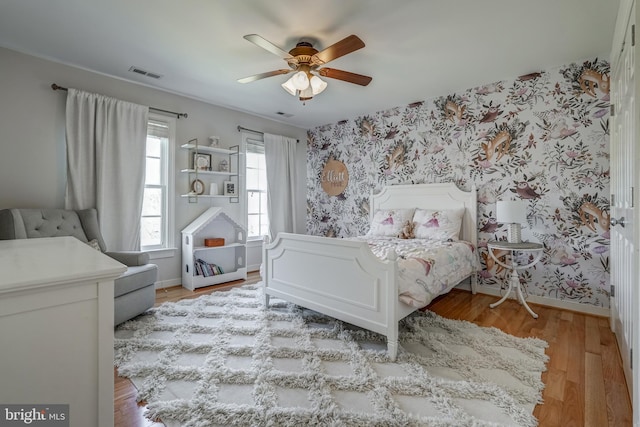 bedroom with light wood-style floors, visible vents, baseboards, and wallpapered walls