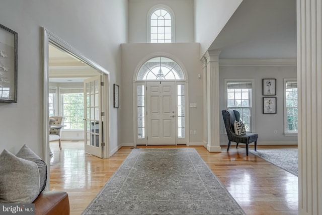 foyer with a healthy amount of sunlight, light wood finished floors, and ornate columns