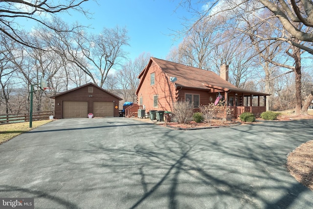 view of side of property with a chimney, a detached garage, an outbuilding, covered porch, and fence