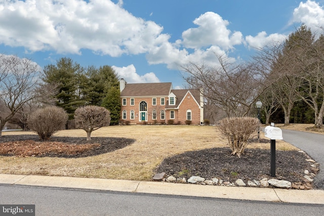 view of front of house featuring brick siding, a chimney, and a front lawn