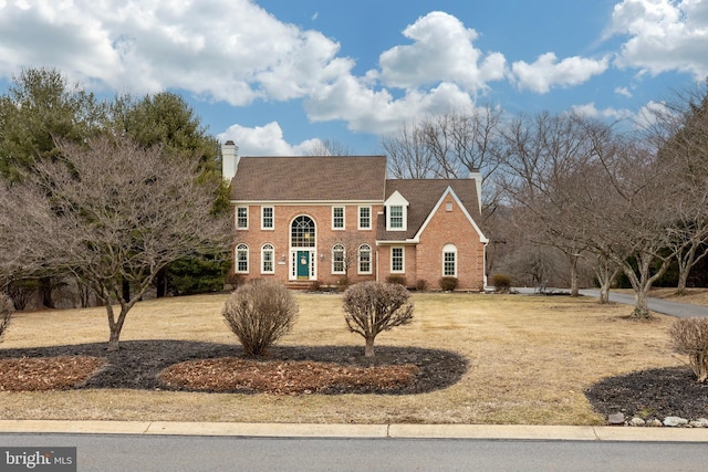 view of front of house with brick siding, a chimney, and a front yard