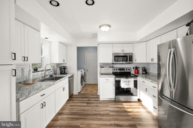 kitchen featuring tasteful backsplash, wood finished floors, washing machine and clothes dryer, stainless steel appliances, and a sink