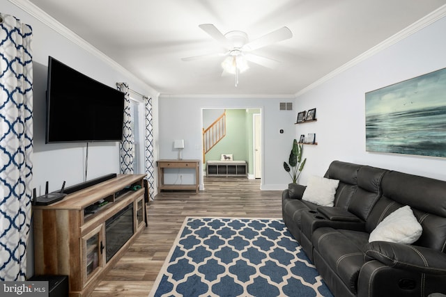 living room featuring wood finished floors, visible vents, a ceiling fan, stairs, and ornamental molding