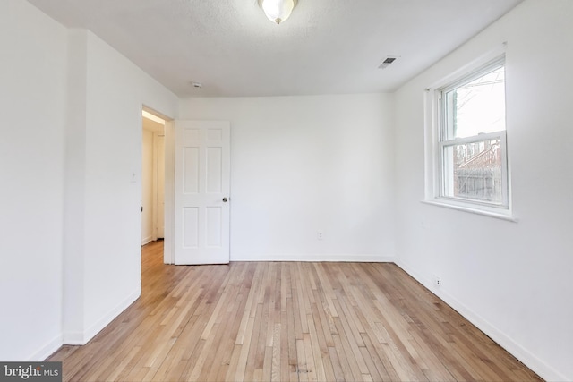 spare room featuring light wood-type flooring, visible vents, and baseboards