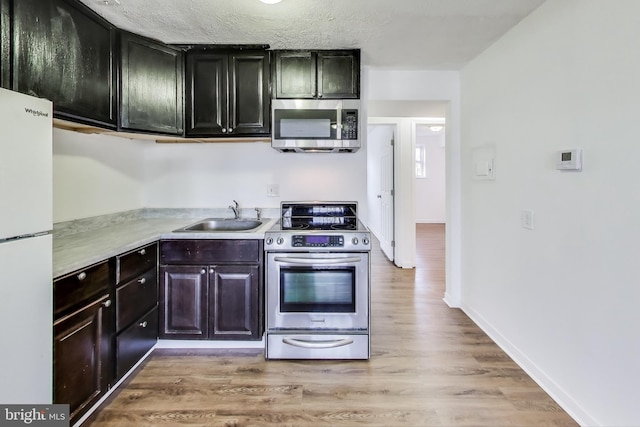 kitchen featuring baseboards, stainless steel appliances, light countertops, light wood-type flooring, and a sink