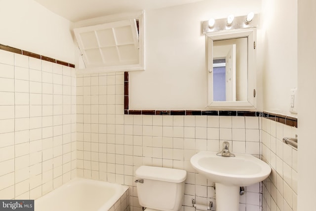 bathroom featuring a washtub, a wainscoted wall, tile walls, and toilet