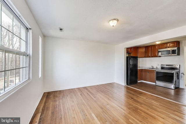 kitchen featuring light wood finished floors, appliances with stainless steel finishes, brown cabinetry, and a wealth of natural light