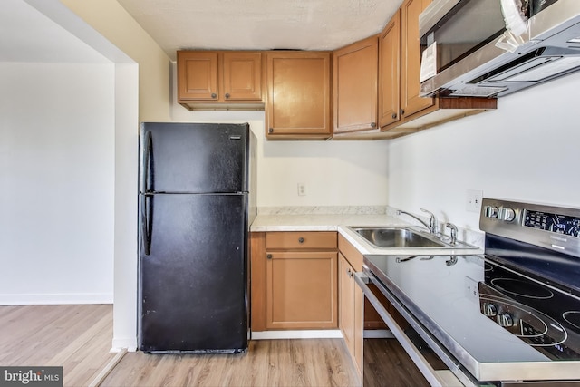 kitchen featuring brown cabinetry, appliances with stainless steel finishes, light countertops, light wood-type flooring, and a sink