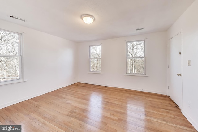 spare room with light wood finished floors, visible vents, and baseboards