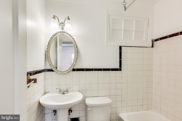 full bathroom featuring toilet, tile walls, a sink, and wainscoting