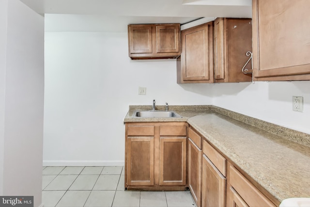 kitchen with light countertops, brown cabinetry, light tile patterned flooring, a sink, and baseboards