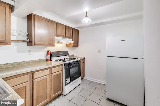 kitchen featuring light tile patterned floors, under cabinet range hood, range with gas stovetop, light countertops, and freestanding refrigerator