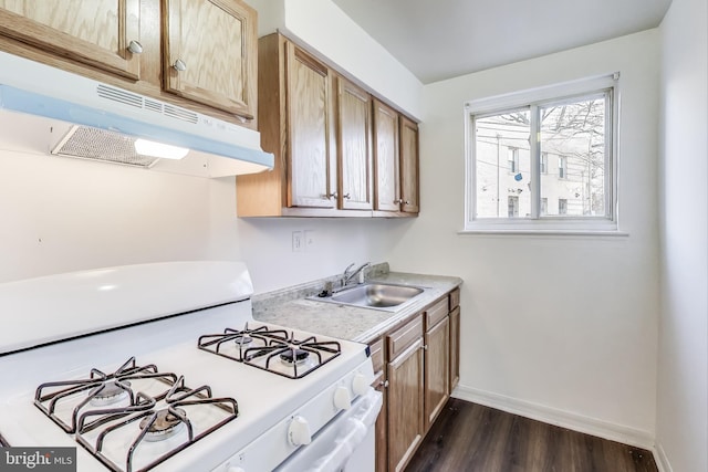 kitchen with dark wood-type flooring, light countertops, white gas stove, under cabinet range hood, and a sink