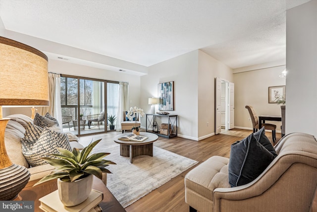 living area with visible vents, a textured ceiling, baseboards, and wood finished floors