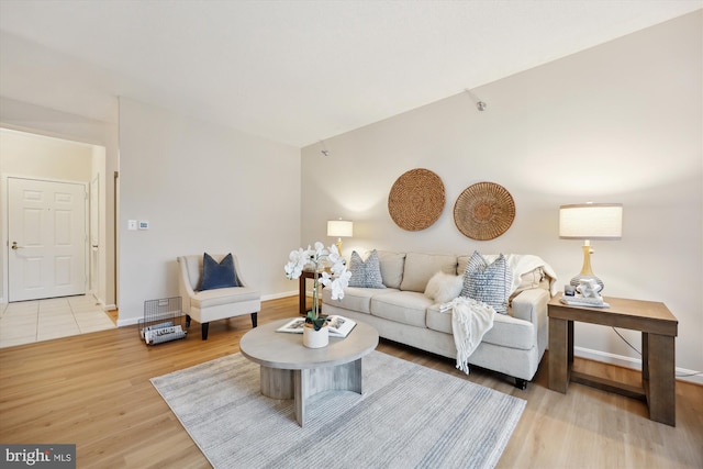 living area featuring light wood-style floors, visible vents, baseboards, and vaulted ceiling