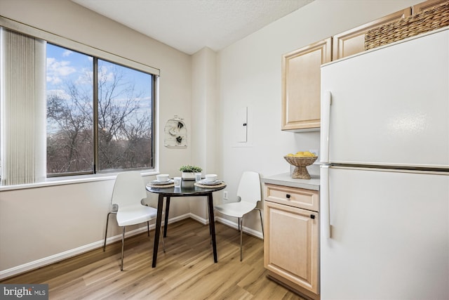 dining area with breakfast area, baseboards, a textured ceiling, and light wood finished floors