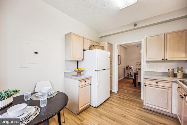 kitchen with light brown cabinetry, light countertops, freestanding refrigerator, and light wood-style floors