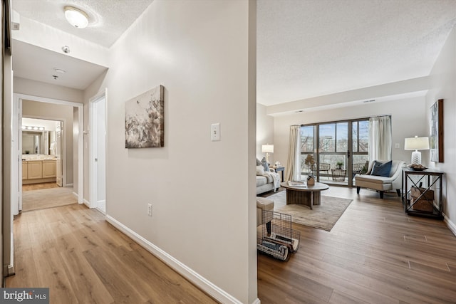 hallway with a textured ceiling, wood finished floors, and baseboards