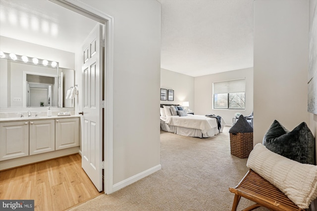 bedroom with light colored carpet, a sink, baseboards, light wood-style floors, and ensuite bath