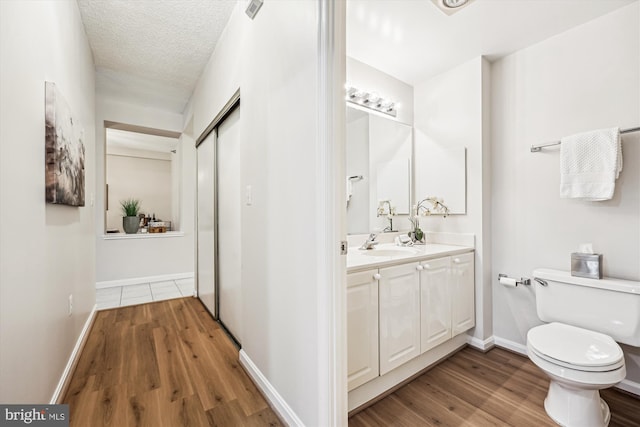 bathroom with toilet, a textured ceiling, wood finished floors, and vanity