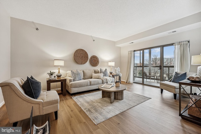 living room featuring a textured ceiling, light wood-type flooring, and visible vents