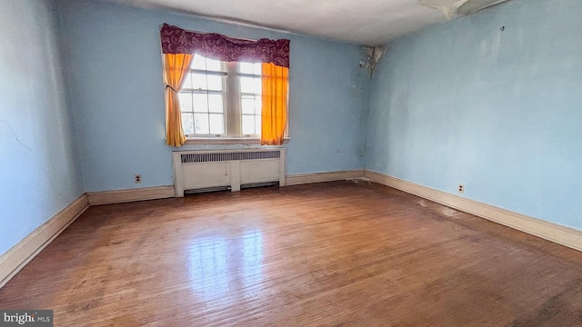 unfurnished room with baseboards, radiator heating unit, and wood finished floors