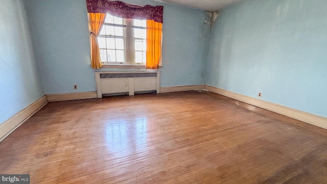 empty room with baseboards, wood finished floors, and radiator