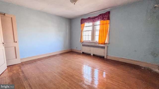 spare room with radiator, baseboards, and wood finished floors