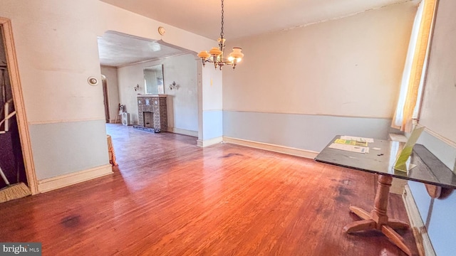 interior space featuring a brick fireplace, a notable chandelier, baseboards, and wood finished floors