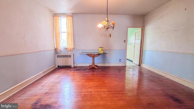 unfurnished dining area with an inviting chandelier, radiator heating unit, baseboards, and wood finished floors