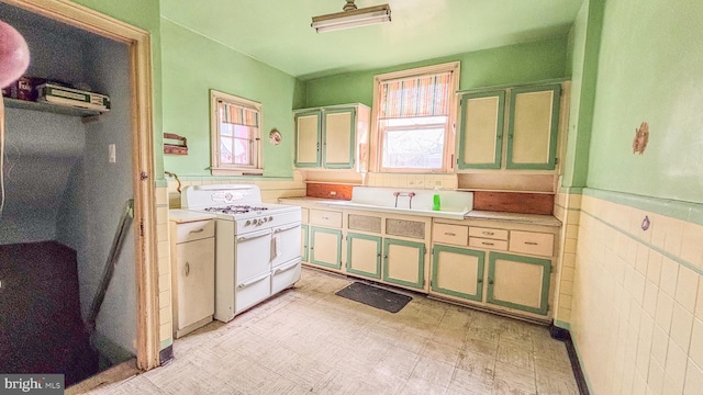 kitchen featuring light floors, a healthy amount of sunlight, wainscoting, and double oven range