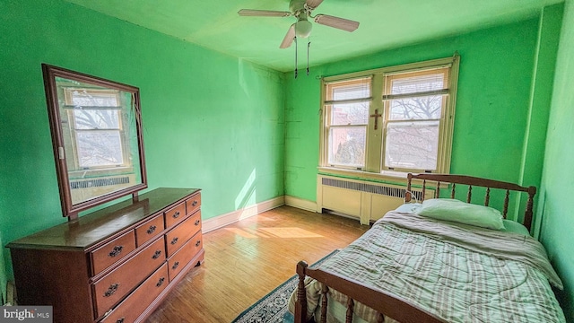 bedroom featuring light wood finished floors, radiator heating unit, baseboards, and ceiling fan