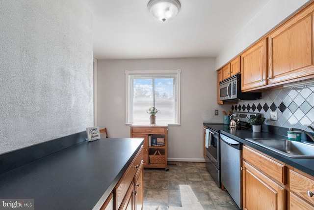 kitchen featuring baseboards, dark countertops, appliances with stainless steel finishes, a sink, and backsplash