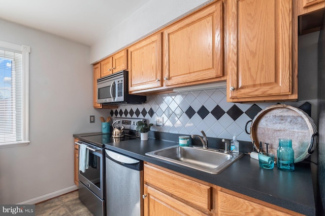 kitchen with a sink, baseboards, appliances with stainless steel finishes, backsplash, and dark countertops