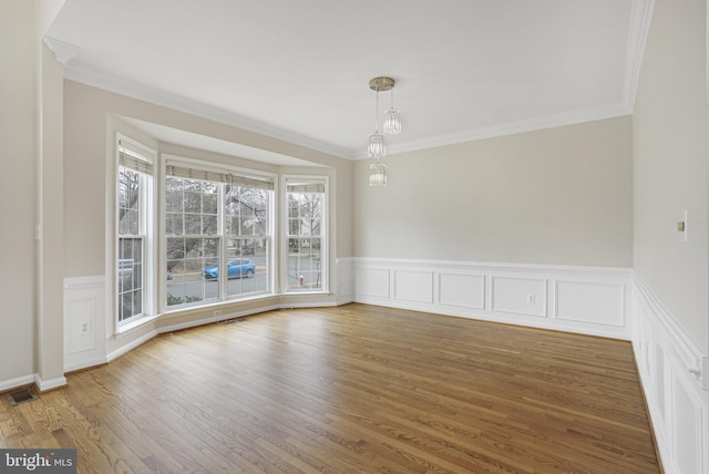 unfurnished dining area with a wainscoted wall, wood finished floors, visible vents, and crown molding