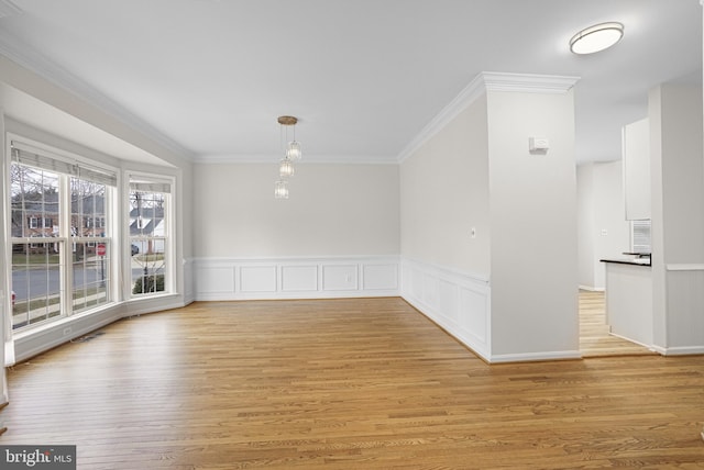 unfurnished dining area featuring light wood-style flooring, a decorative wall, crown molding, and wainscoting