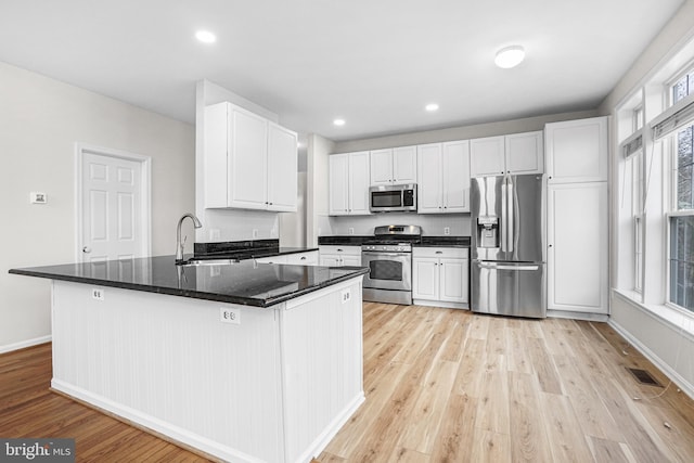 kitchen with appliances with stainless steel finishes, white cabinetry, a sink, light wood-type flooring, and baseboards