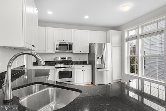 kitchen featuring appliances with stainless steel finishes, dark stone counters, white cabinets, and a sink