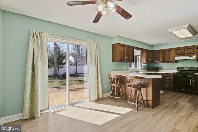 kitchen with black gas range oven, visible vents, light countertops, dark brown cabinets, and under cabinet range hood