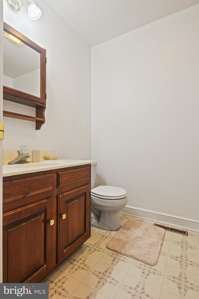 half bathroom featuring vanity, baseboards, visible vents, tile patterned floors, and toilet