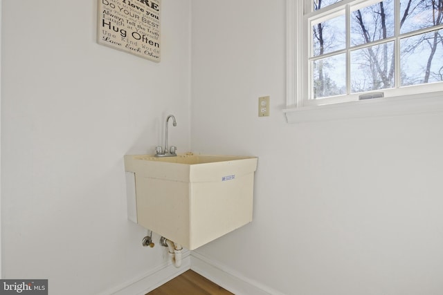 clothes washing area featuring wood finished floors, baseboards, and a sink